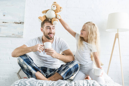 微笑的小女儿玩玩具熊，而快乐的父亲在卧室喝茶