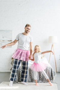 快乐的父亲和可爱的小女儿穿着粉红色的Tut裙，牵着手在家跳舞