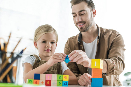 微笑的父亲和可爱的小女儿在家用五颜六色的立方体学习数学