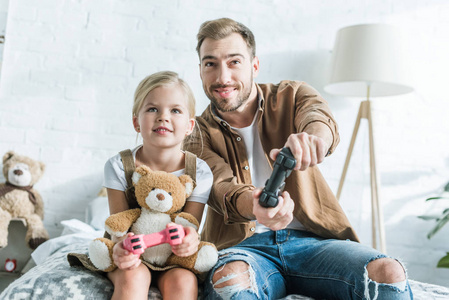 快乐的父亲和可爱的小女儿带着泰迪熊在家玩操纵杆