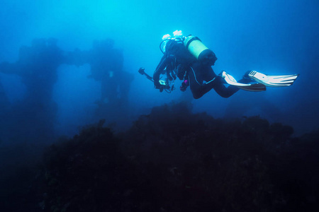 潜水员用他的相机潜入蓝海向沉船俯冲。船上的旧残骸看上去很遥远，模糊不清，给人一种神秘的感觉