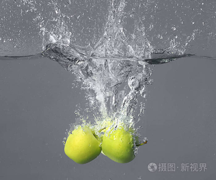在灰色的背景下把苹果掉进水里