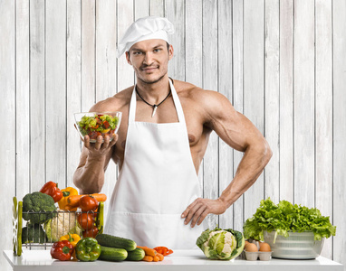 男人在厨房里做健美，穿着白色长袍，煮着保护围裙，调制蔬菜和水果