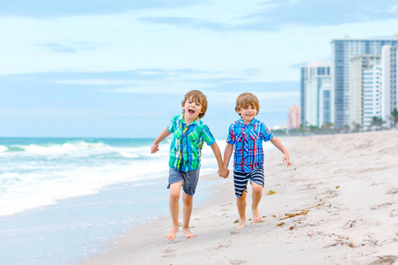 两个快乐的小孩在海边奔跑。有趣的可爱的孩子, 兄弟姐妹和最好的朋友, 在暴风雨多风的日子里度假和享受夏天。健康的孩子在迈阿密的海