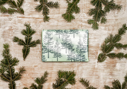 一种礼物，用节日的圣诞纸包裹在木制背景上，有新鲜的树枝。 顶部视图复制空间平躺。