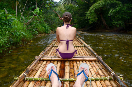 女孩坐在竹筏上。 在丛林里的河里漂流。 背面视图