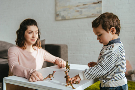妈妈和小儿子在家里客厅的桌子上玩玩具恐龙的选择性焦点