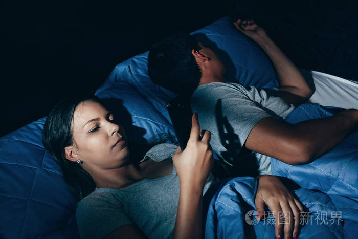 躺在床上的年轻夫妇.人睡觉时一名年轻的女子,看着夜晚的电话