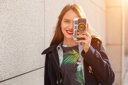 快乐的嬉皮士女孩在城市街道上用复古相机拍照。太阳耀斑