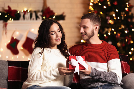 在圣诞树附近的家里给年轻女人送礼物的男人照片
