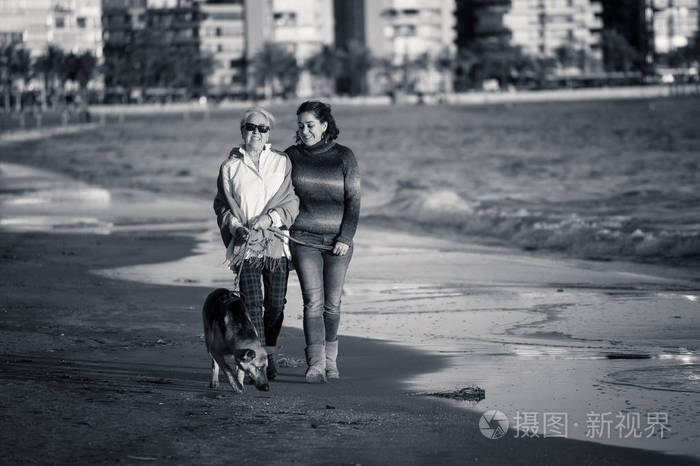 快乐的高级母亲，她的成年女儿和德国谢帕德狗花时间在日落光的海滩上散步，在幸福的家庭时刻，宠物动物享受狗友好的旅游和退休。
