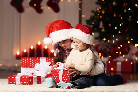 美丽的两个姐姐，带着礼品盒坐在家中的圣诞树旁