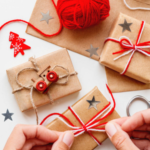 女人正在用手工纸包装圣诞节和新年DIY礼物。 用线绑着的礼物。 白色背景上的红色心脏和圣诞树符号。