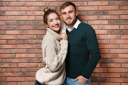 一对年轻夫妇在砖墙附近穿暖和的毛衣