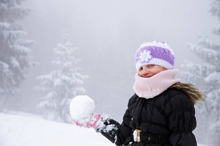 冬天的小女孩在白雪覆盖的森林里玩雪球