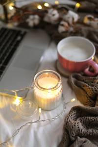床上的热卡布奇诺杯。 家居装饰。 玻璃罐子里的蜡烛格子棉笔记本电脑。 很舒服。 秋天。