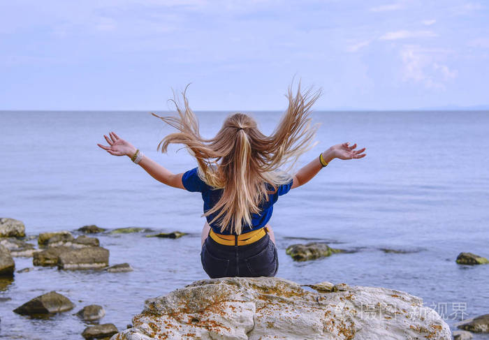 一个穿着蓝色夹克的女孩她的头发朝下坐在平静的海