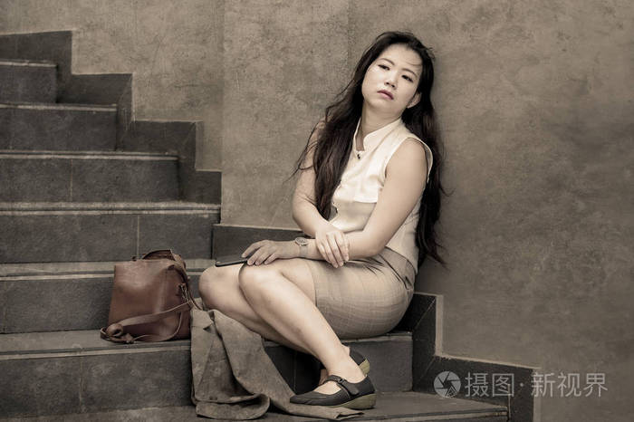 年轻的沮丧和绝望的亚洲女商人独自哭泣,坐在街道楼梯上,承受着压力和
