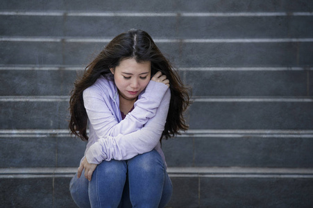 年轻的悲伤和沮丧的亚洲学生妇女或被欺负的青少年坐在户外的街道楼梯上，不知所措，焦虑地感到绝望，患有抑郁症