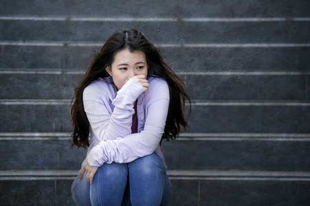 年轻的悲伤和沮丧的亚洲学生妇女或被欺负的青少年坐在户外的街道楼梯上，不知所措，焦虑地感到绝望，痛苦抑郁症