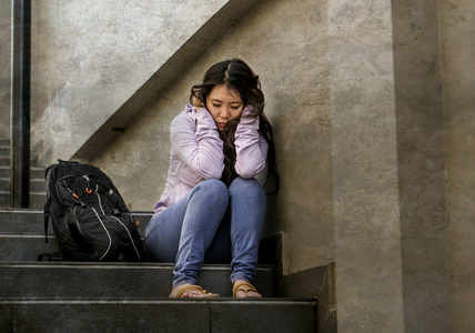 年轻的悲伤和沮丧的亚洲学生妇女或被欺负的青少年坐在户外的街道楼梯上，不知所措，焦虑地感到绝望，患有抑郁症