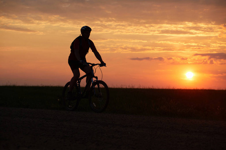 日落背景下骑自行车的剪影。比克尔晚上骑在路上。室外红黄色背景