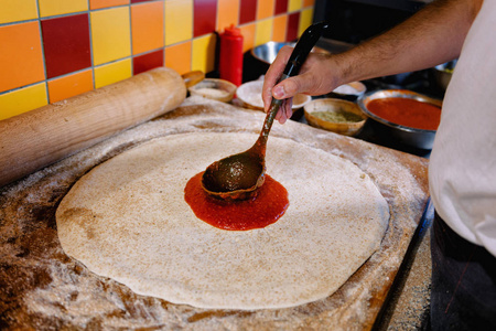 厨师在披萨店用金属瓢在披萨面团上撒番茄酱。 披萨制作过程。