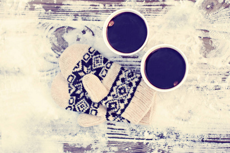 在冬天，两个纸工艺品玻璃杯和一杯热饮料咖啡可可覆盖葡萄酒和白色和黑色手套在户外的桌子上。 冬季时间概念。 沐浴在寒冷中。