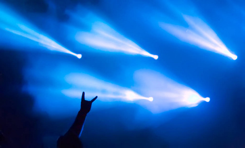 手显示重金属岩石标志的角与蓝色舞台灯与蓝色舞台灯的背景，在金属如何开放空气节在拉脱维亚。