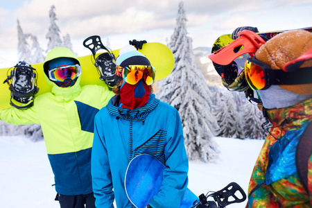 三个滑雪者在滑雪场散步。朋友们带着滑雪板爬到山顶, 穿过森林, 穿着反光护目镜, 穿着五颜六色的时尚服装