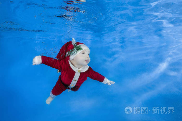 婴儿在蓝色的水背景下在游泳池里游泳.