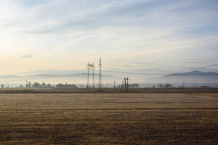 罗马尼亚人日出时空田。 背景上的高压电力线。 从公共汽车窗口查看。 天空中温暖的太阳。 布拉索夫县