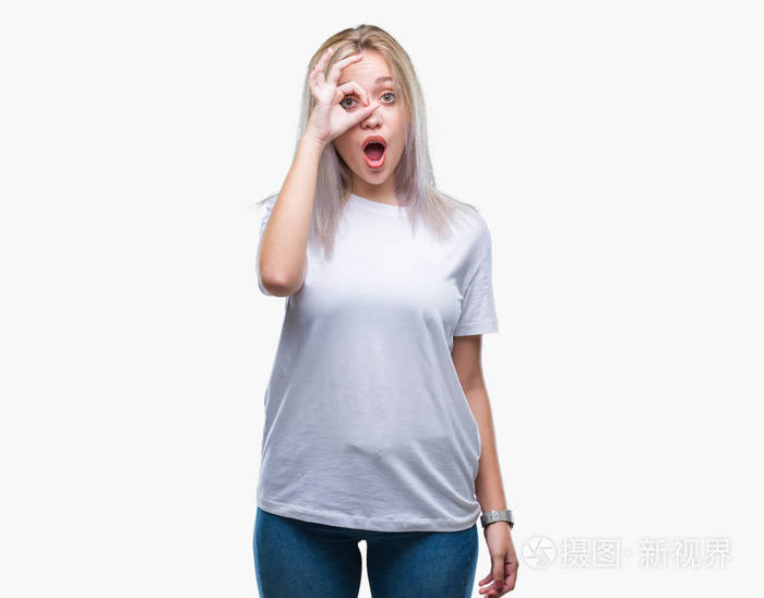 年轻的金发女人在孤立的背景下做着ok的手势,惊讶的脸眼睛透过手指