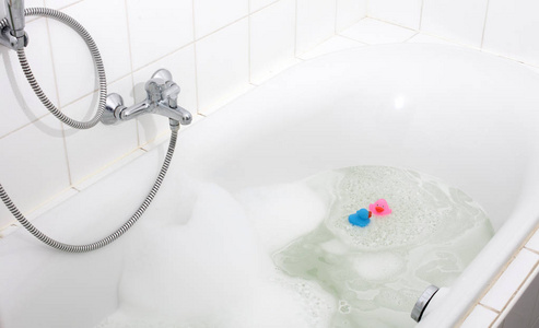 粉红色和蓝色的鸭子在浴缸里，周围是肥皂