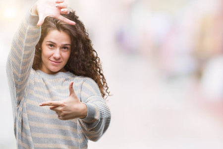 美丽的黑发卷发年轻女孩穿着冬季毛衣，在孤立的背景上微笑，用手和手指制作框架，带着快乐的脸。 创造力和摄影理念。