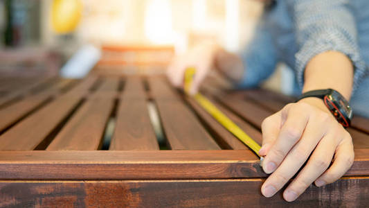 年轻的亚洲男人用卷尺测量陈列室的木制户外桌子。 用于家居装修的购物家具。 室内设计概念