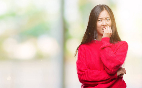 年轻的亚洲女人穿着冬天的毛衣，穿着孤立的背景，看上去压力很大，紧张，双手咬着嘴的指甲。 焦虑问题。