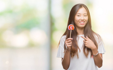 年轻的亚洲女人在孤立的背景下吃棒棒糖，很高兴用手和手指指指点点