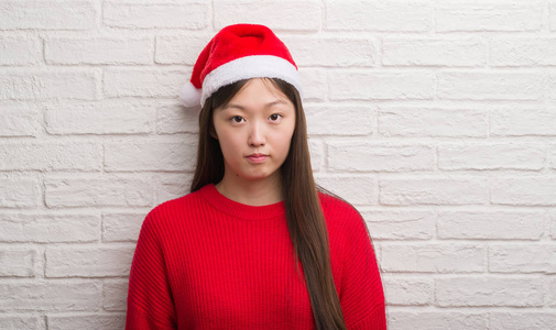 年轻的中国女人戴着圣诞老人的帽子，脸上有自信的表情，思维严肃