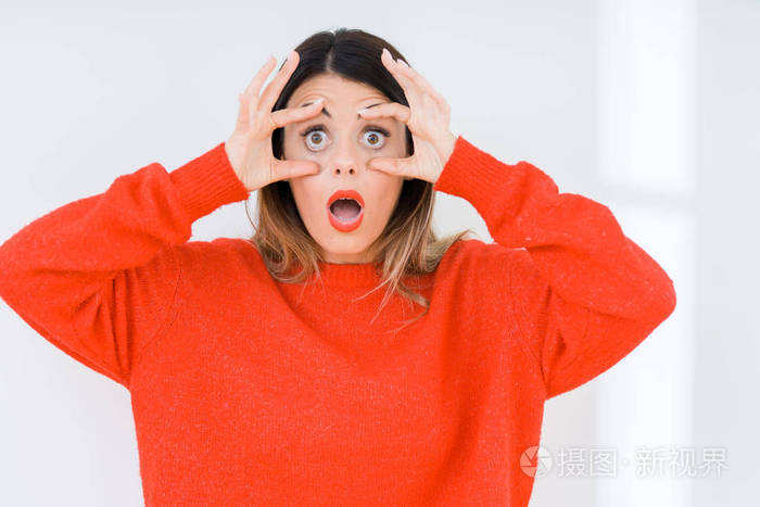 年轻的女人穿着休闲的红色毛衣在与世隔绝的背景下试图睁开眼睛手指