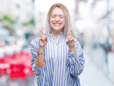 年轻的金发女人在孤立的背景上微笑着交叉手指与希望和眼睛闭上。 运气和迷信的概念。