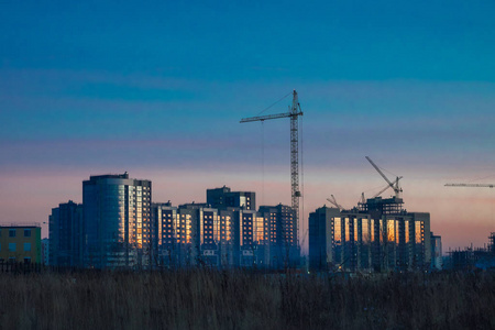 建筑起重机和正在建造的现代建筑对抗夜空。 日落的天空。