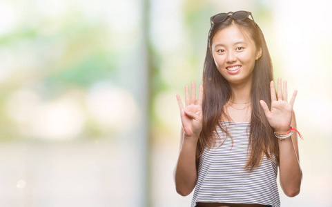 年轻的亚洲女人戴着太阳镜，在孤立的背景上，用手指数字9，同时微笑，自信和快乐。