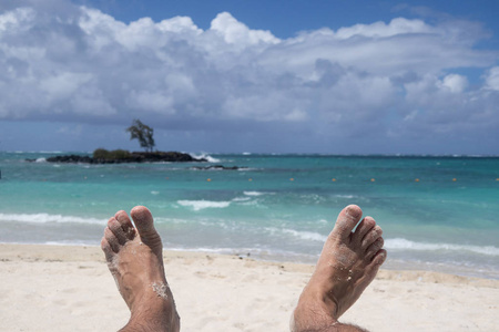 一个人的脚躺在沙滩上，天堂象征着幸福和节日