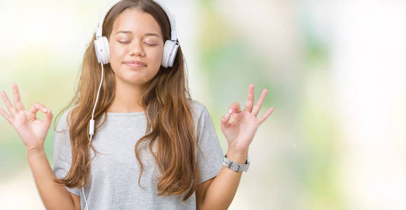 年轻漂亮的女人戴着耳机，在孤立的背景上听音乐，放松，闭着眼睛微笑，用手指做冥想手势。 瑜伽概念。