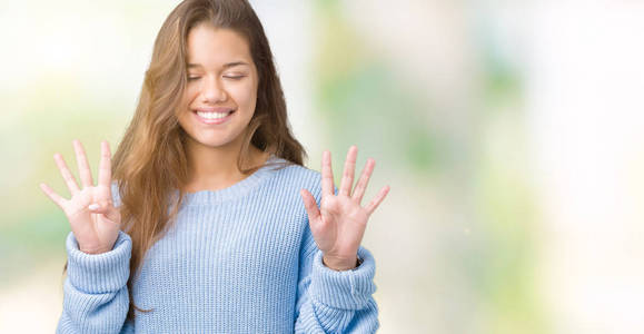 年轻漂亮的黑发女人穿着蓝色的冬季毛衣，在孤立的背景下，用手指举着九号，微笑着自信和快乐。