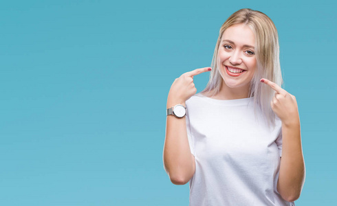 年轻的金发女人在孤立的背景上微笑,自信地展示和手指,牙齿和嘴.