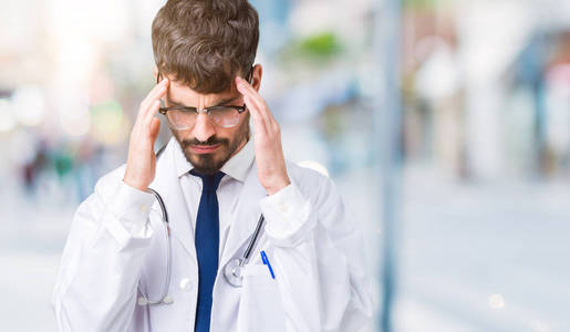 年轻的医生穿着医院外套，在孤立的背景上，手在头上，因为压力而疼痛。 偏头痛。
