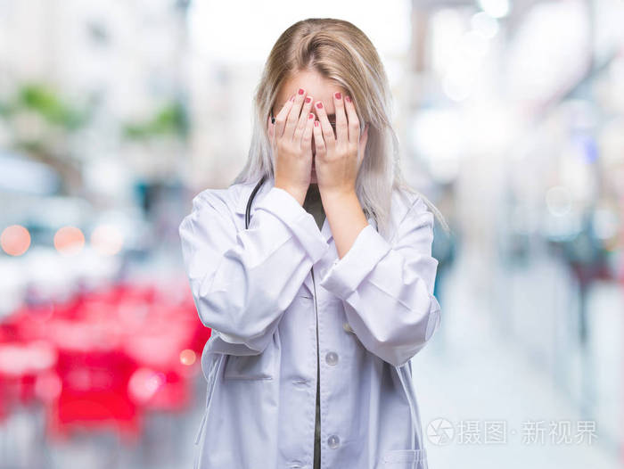 年轻的金发医生女人在孤立的背景上悲伤的表情覆盖着脸用手哭泣抑郁的