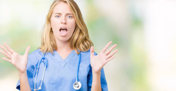 美丽的年轻医生女人穿着医疗制服，在孤立的背景下疯狂疯狂地大喊大叫，咄咄逼人的表情和手臂抬起。 挫折概念。